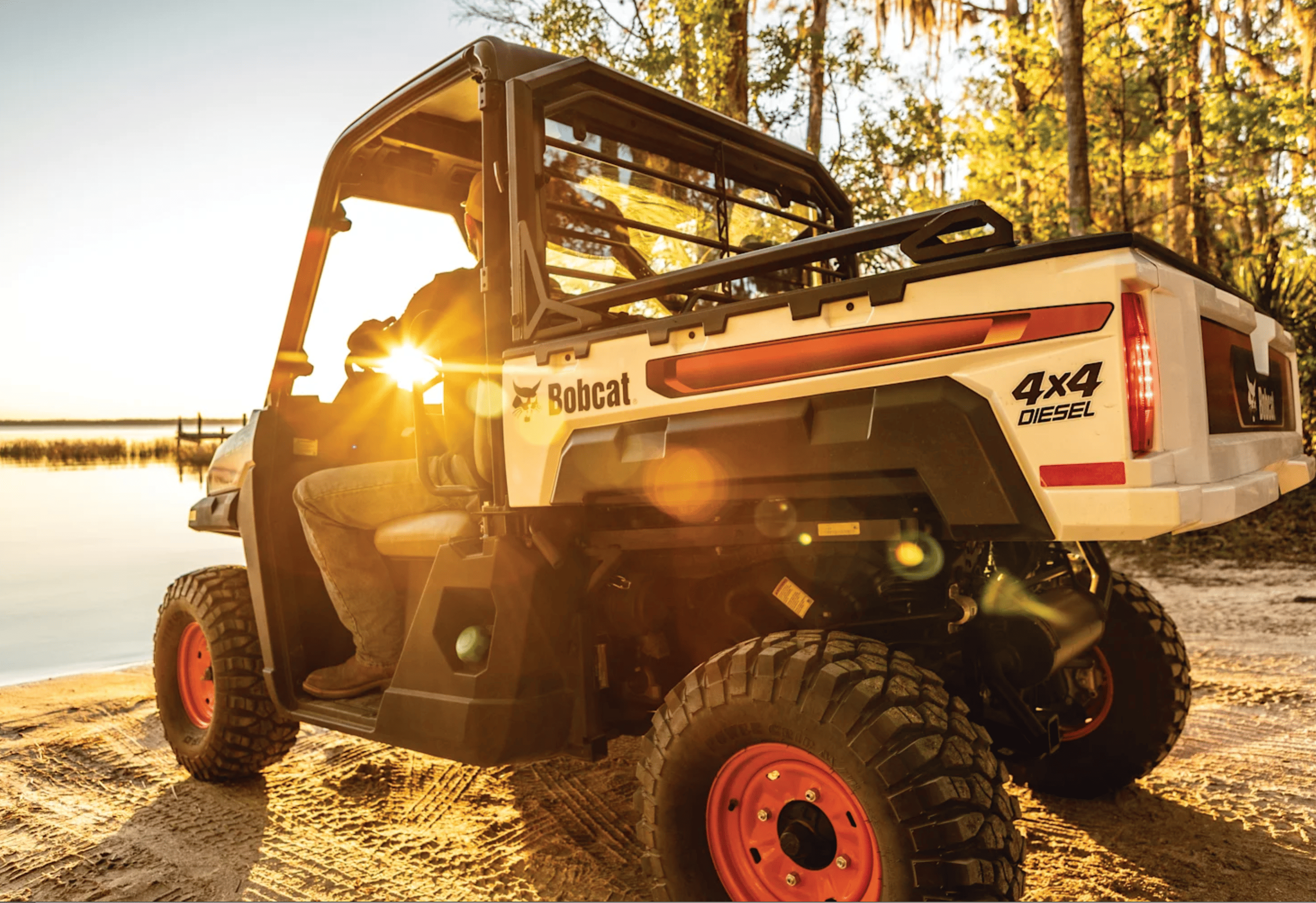 A 2024 Bobcat® Utility Vehicles UV34 Diesel parked on a sandy beach, showcasing its rugged design against a backdrop of waves and blue sky.