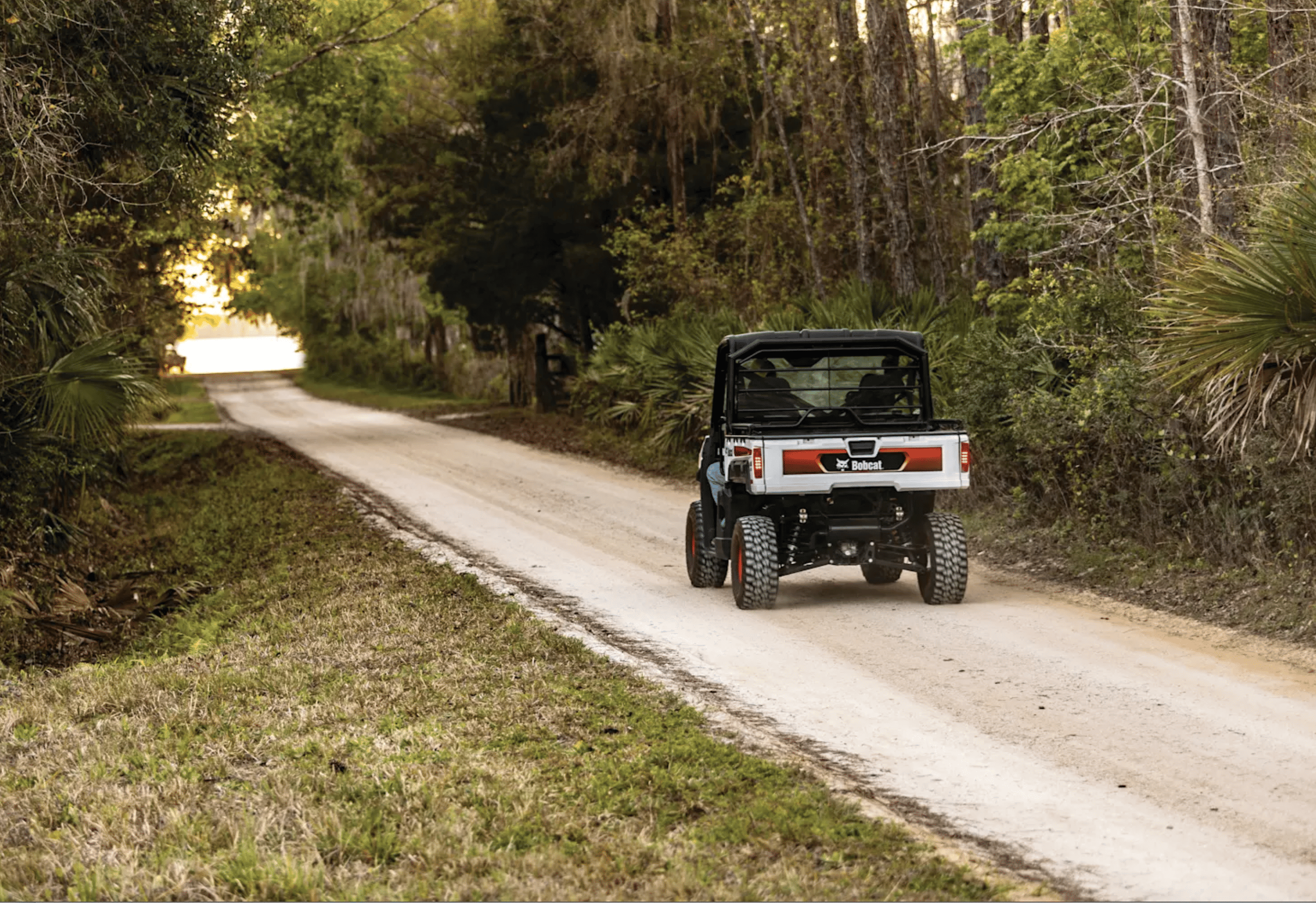 A 2024 Bobcat® Utility Vehicle UV34 Diesel driving along a dirt road, highlighting its capability for off-road adventures.