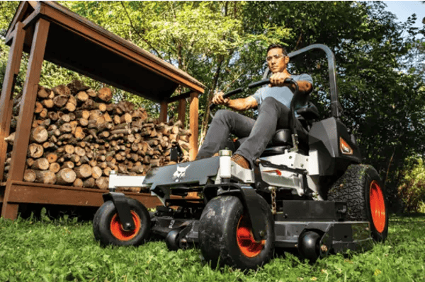 A man operates a 2025 Bobcat® ZT3500 Zero-Turn Mower with a 61” deck in a well-maintained yard.