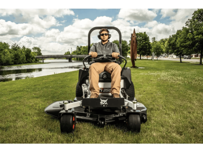 A man confidently rides a Bobcat® ZT3500 Zero-Turn Mower, expertly navigating lush green grass with a 61” deck.