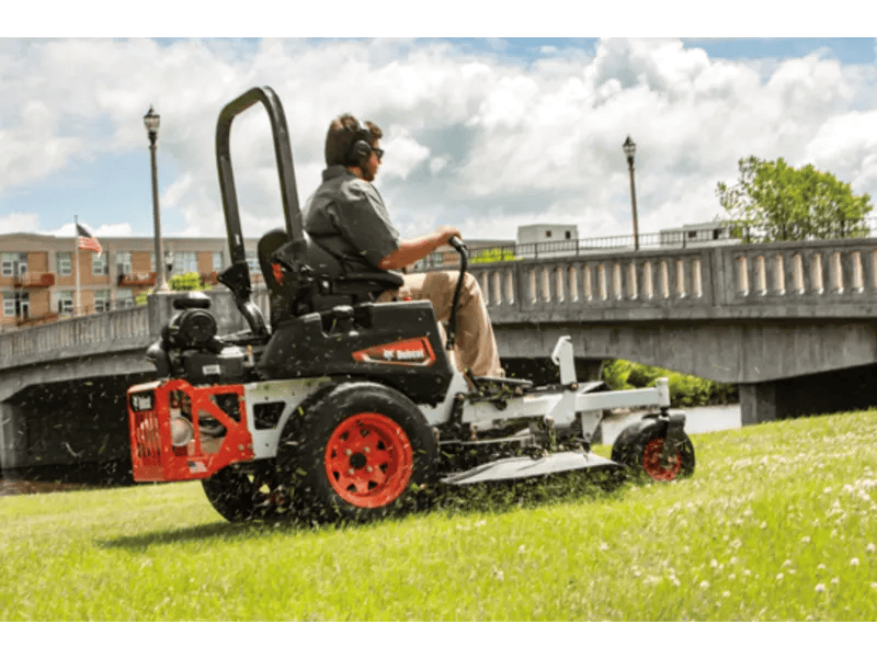 A man operates a sleek black and red Bobcat® ZT3500 Zero-Turn Mower, featuring a 61” deck, as he mows the lawn.