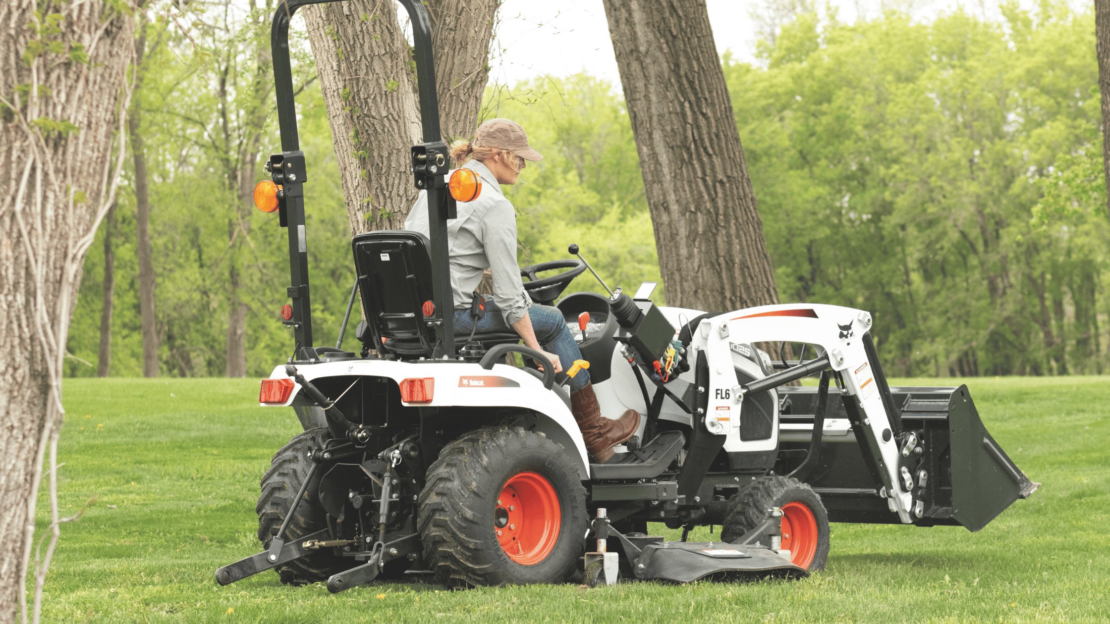 A woman rides a Bobcat® CT1025 Sub-Compact Tractor through lush grass in Greenville, NY, showcasing its versatility.