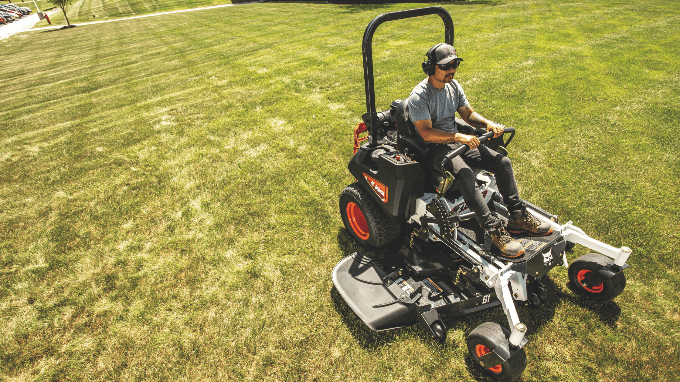 A man confidently rides a black and red Bobcat® ZT6100 Zero-Turn Mower in Greenville, NY, showcasing its power and precision.