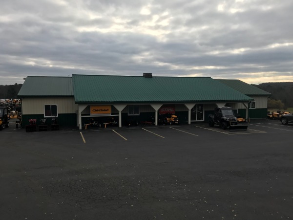 Greene County Power Equipment store in Greenville, NY features a green metal roof and beige siding, with Cub Cadet and STIHL signage displayed above outdoor power equipment. The parking lot in front is mostly empty, except for a black utility vehicle parked near the entrance under an overcast sky.