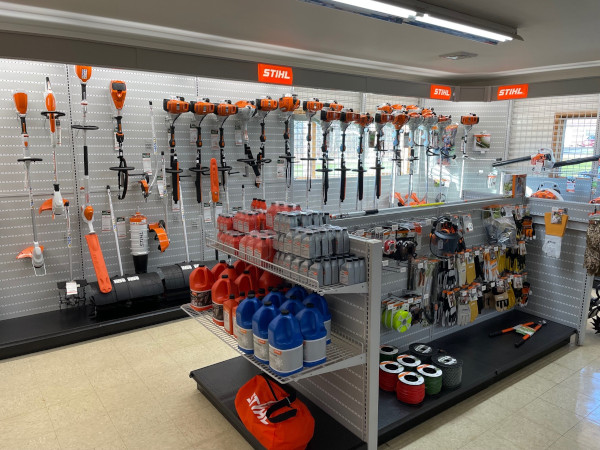 "A well-stocked STIHL display inside Greene County Power Equipment in Greenville, NY, featuring a variety of trimmers, chainsaws, and other handheld power tools mounted on a pegboard wall. Shelves in the foreground hold fuel cans, oil, safety gear, and accessories, all neatly arranged under bright STIHL signage.