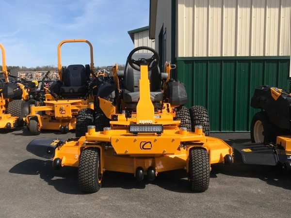 A bright yellow Cub Cadet zero-turn mower is displayed outside Greene County Power Equipment in Greenville, NY, with additional mowers lined up in the background against a beige and green metal building. The mower features a sturdy frame, wide cutting deck, and a high-backed seat for operator comfort under a clear blue sky.