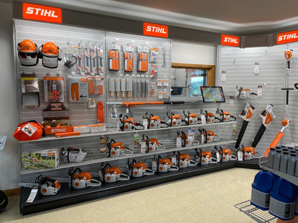 An organized STIHL display inside Greene County Power Equipment in Greenville, NY, showcasing a variety of chainsaws, trimmers, protective gear, and accessories. The bright orange and white STIHL branding stands out against the pegboard wall, with shelves neatly stocked with outdoor power tools and maintenance supplies.